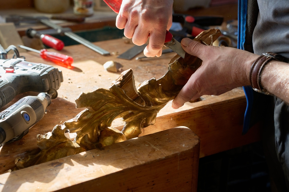 Woodworker carving an ornate piece by hand at a sunlit bench